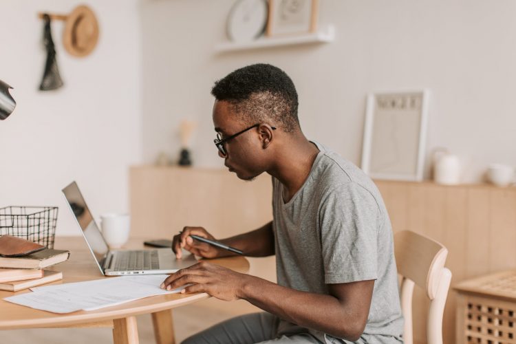man in gray t shirt holding a pen while using laptop